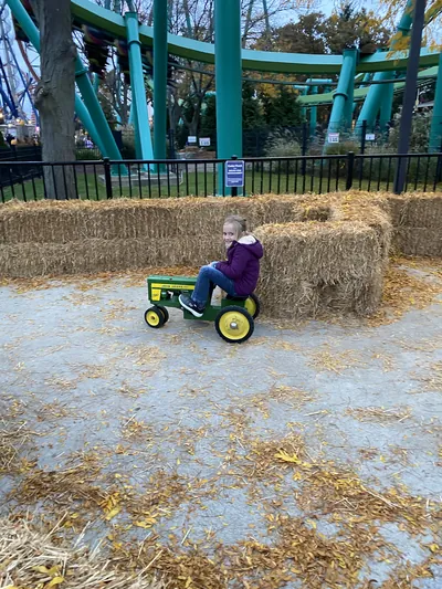 A child pedalling a toy tractor through the straw-bale maze at Cedar Point, with coaster track behind