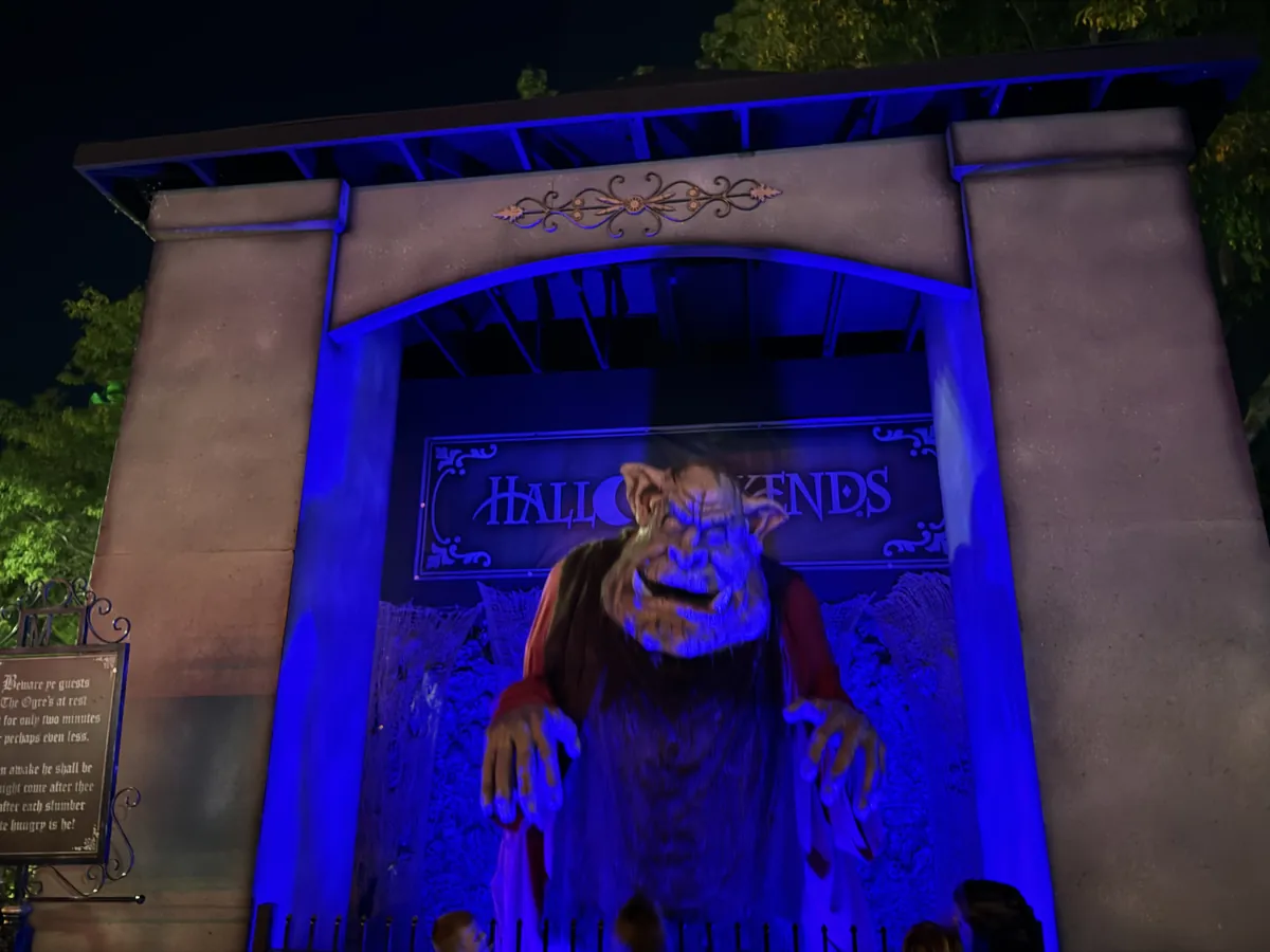 A HalloWeekends archway at Cedar Point lit blue at night, with a hunched ogre figure reaching out from under the banner