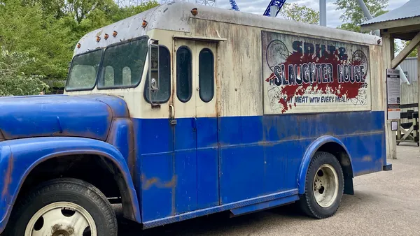 Rusted blue and white Spilt 'n Trails Meat Factory delivery bus parked outside the Slaughter House maze at Cedar Point