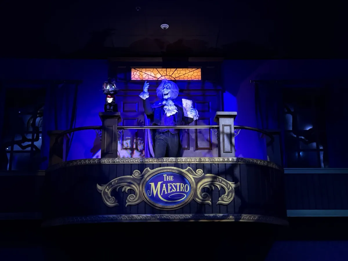 The Maestro animatronic, a Phantom-styled conductor figure, on a balcony stage with his feline sidekick Arpeggio and a glowing 'The Maestro' sign below