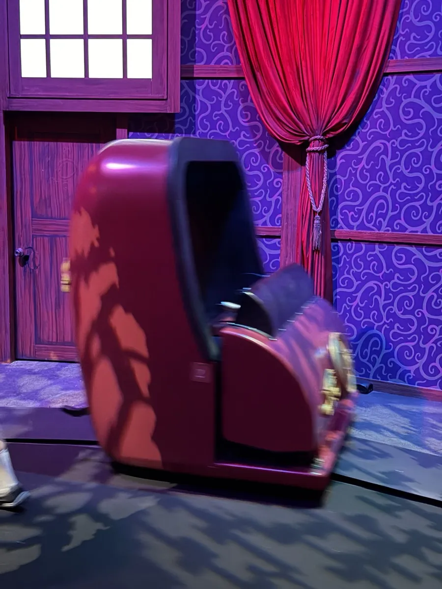 Phantom Theater opera box ride vehicle in a richly themed scene with red velvet rope and purple-patterned wallpaper