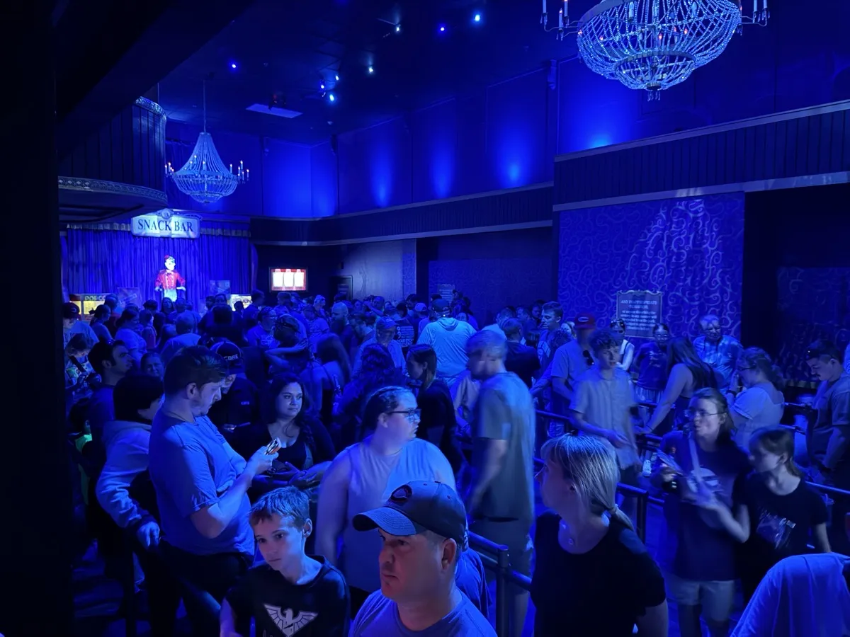 Crowd in the Phantom Theater pre-show lobby illuminated by chandeliers in deep blue light